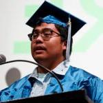 A graduate in cap and gown stands at a podium during a graduation ceremony